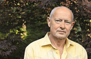 Image: a headshot of Michael Findlay, a distinguished man with white hair wearing a casual yellow button down shirt who stands in front of a maple tree.