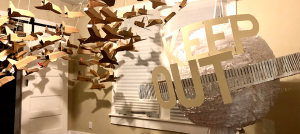 Installation with several cardboard airplanes and the words Keep Out in a room