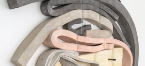 Twisted bars of cement, polyurethane, and foam in pastel colors over a white wall