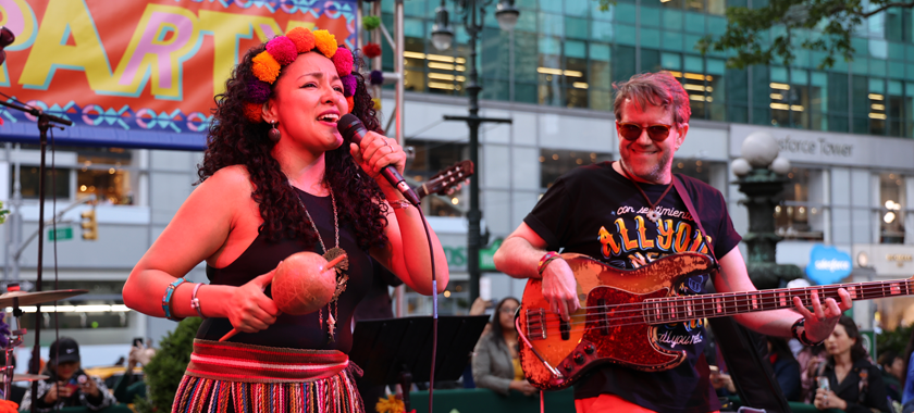 Afro-Andean Funk performing in Quechua during a live concert at Bryant Park, New York. In the photo, the band's leaders, Araceli Poma, Peruvian singer, and Matt Geraghty, bassist and producer, are pictured. Araceli is wearing traditional Peruvian attire.