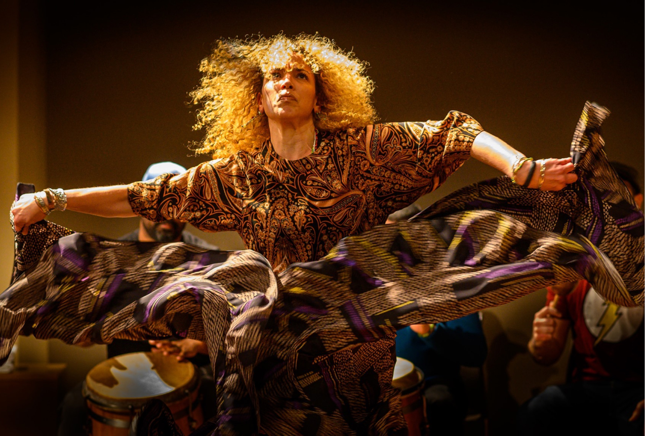 Close up image of a woman dancing. She is dancing and looking towards the sky, in the direction of the camera.