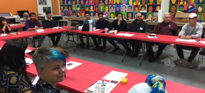Participants in the 2018 Immigrant Artist Mentoring Program: San Antonio, seated around connected rectangular tables in a vibrant gallery setting