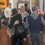 Individuals hugging and talking in a gallery setting