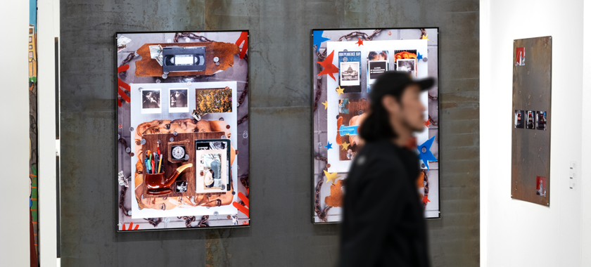 A person walks by an art fair booth displaying large-scale photographic works installed on large steel panels.