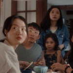 A group of Chinese American people of all ages sitting around the table, looking into the direction of the camera