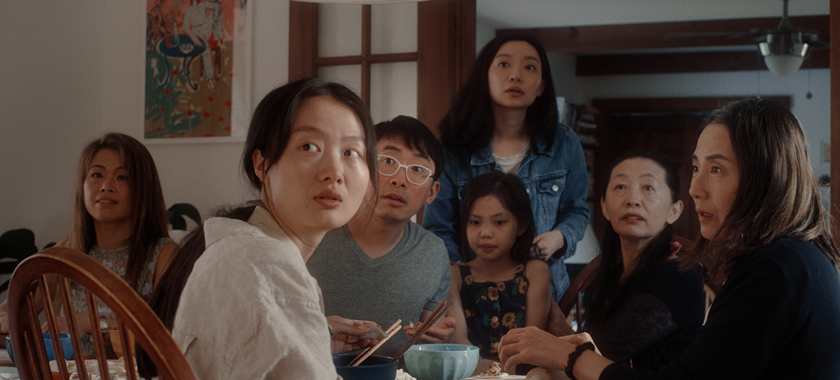 A group of Chinese American people of all ages sitting around the table, looking into the direction of the camera