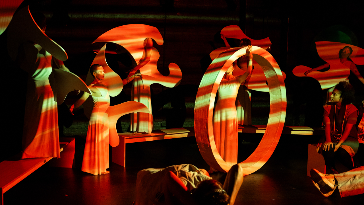 Dancers with life-sized sculptural stage elements on a darkened stage