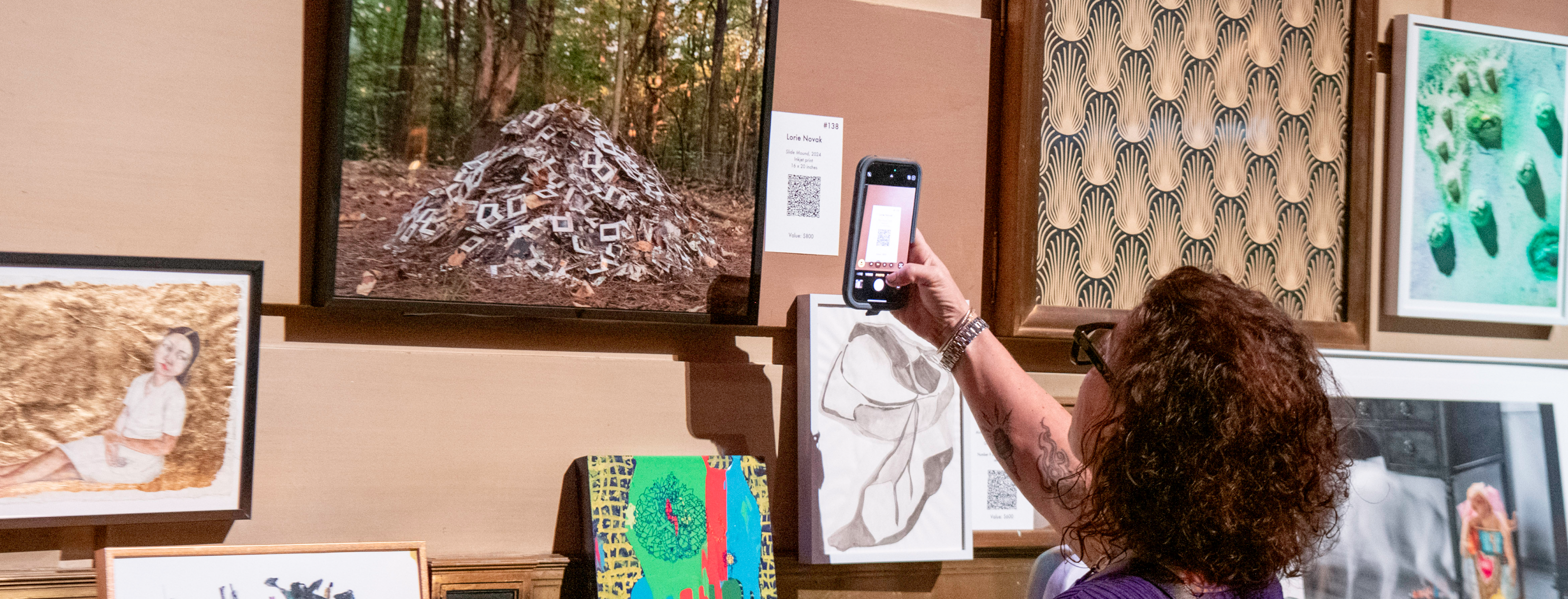 An individual holds their phone up, scanning a QR code next to an artwork that was on display at NYFA's 2025 Hall of Fame Benefit