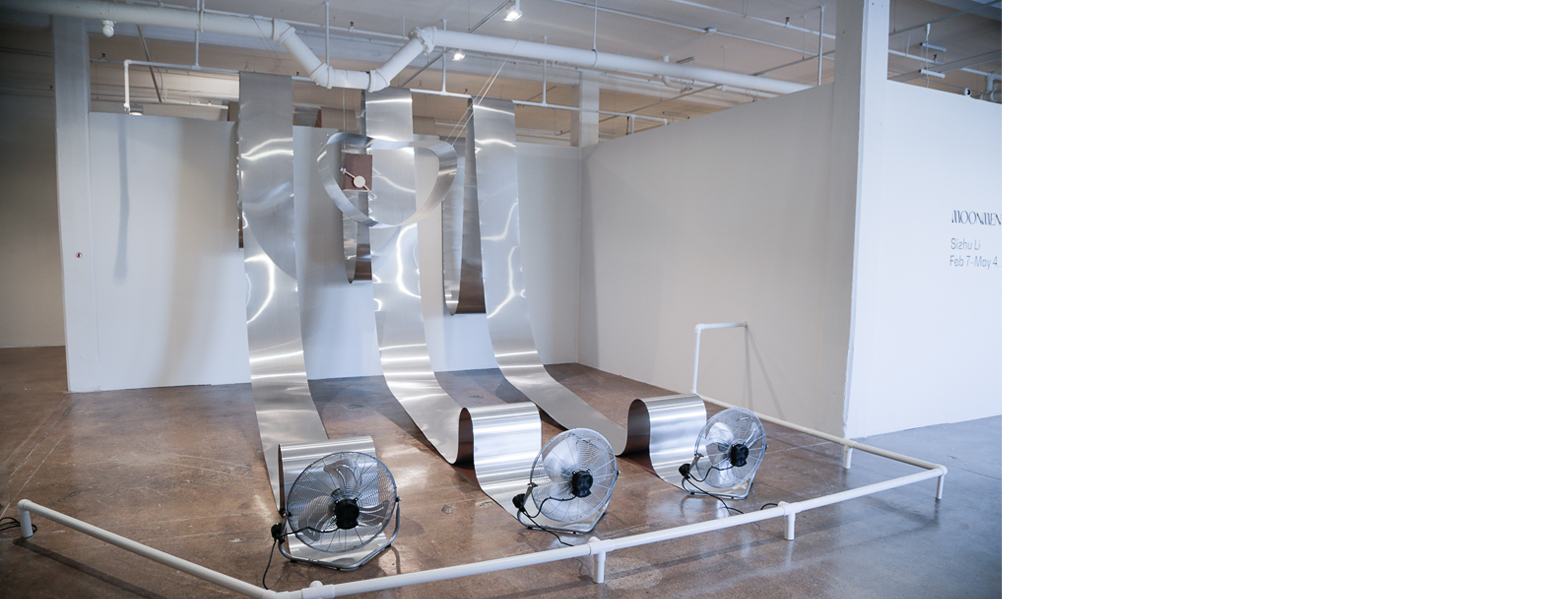 Site-specific installation of aluminum sheets suspended from the ceiling and gracefully rolled down to the ground with fans blowing on them for movement.