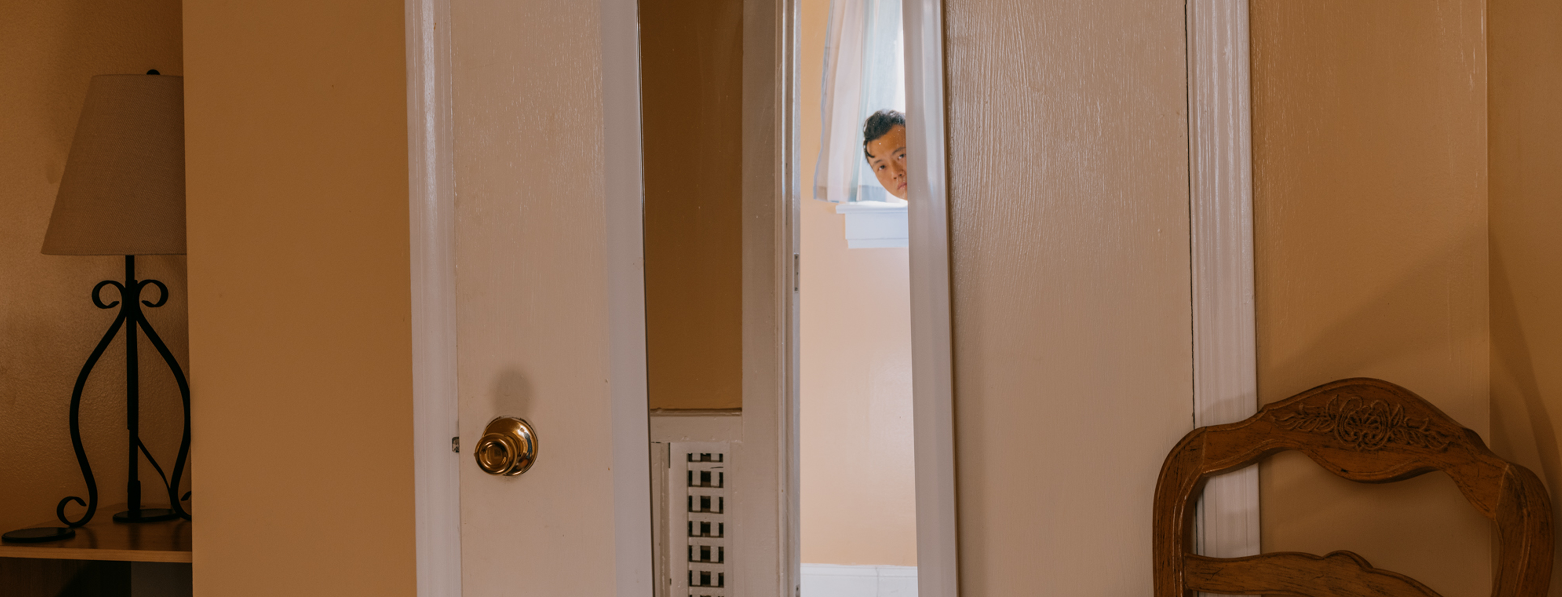 Photograph of an individual in an interior setting, head peeking out from behind a door